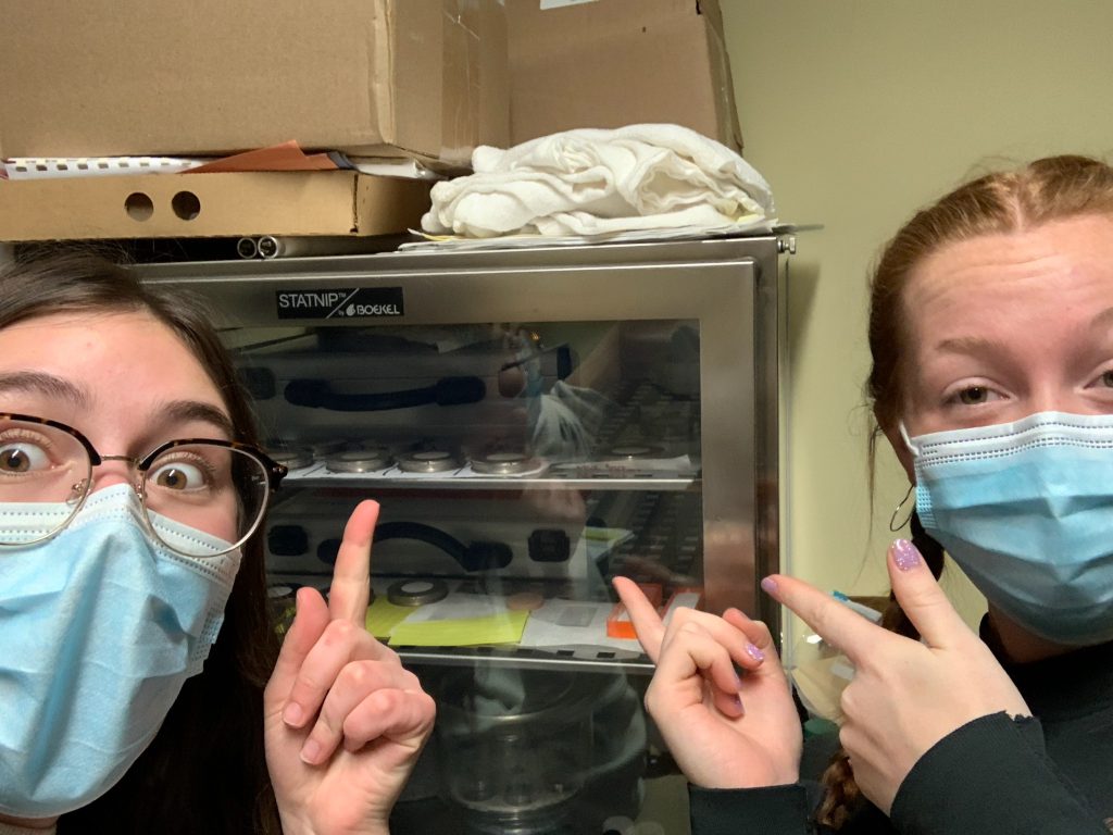 Two women wearing masks pointing to a storage container